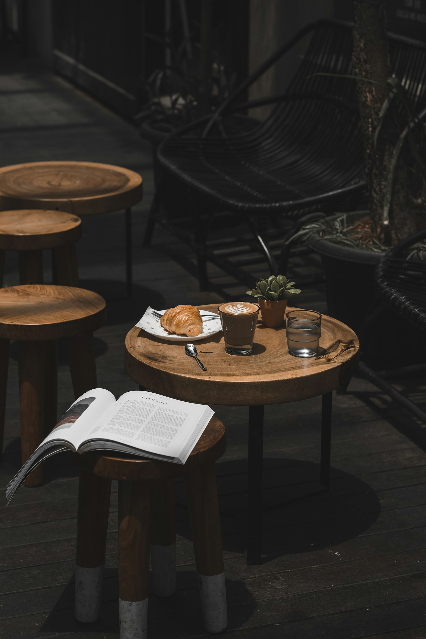 Latte and a croissant on a wooden café table beside an open book
