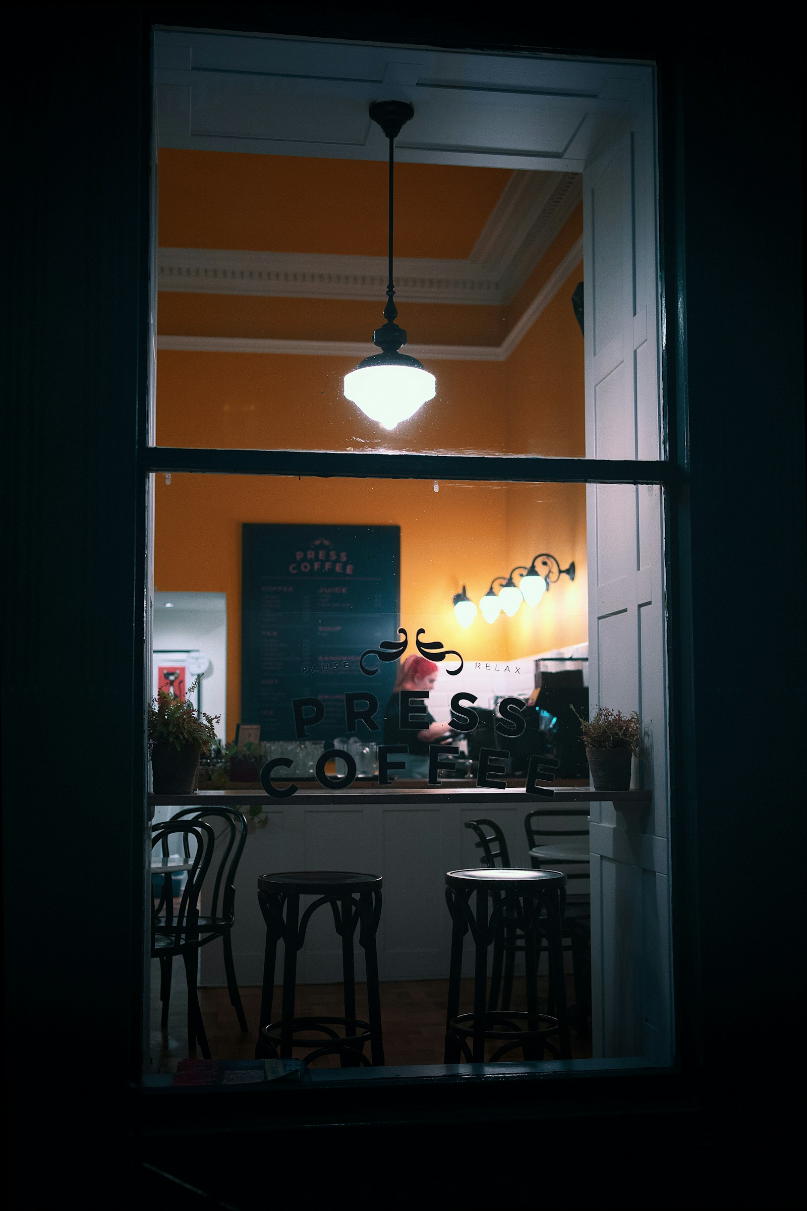 Small tables and stools seen through the window of a warmly lit café